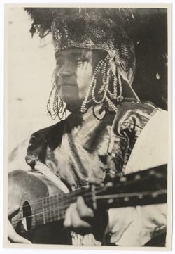 Three-quarter figure shot of Indigenous person in Item 3 above playing a guitar.