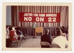 Cesar Chavez speaking in front of banner opposing Proposition 22