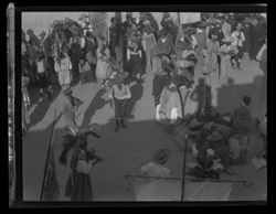 Long shot, from above, of fiesta or ceremony. Indigenous person with guitar, costumed as in Items 1-6 above, at lower right. Crowd of performers and/or spectators in background.